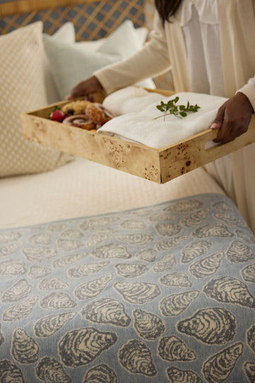 Cream-colored half shell blanket with shell pattern, displayed on bed with food tray held by person in white clothing.4