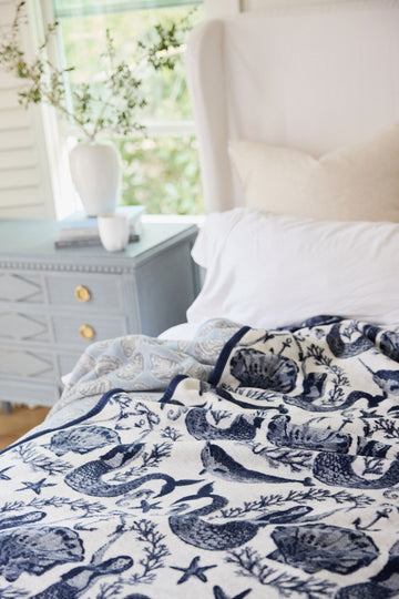 Cream blanket with navy blue sea creatures and coral print, draped on a bed.3