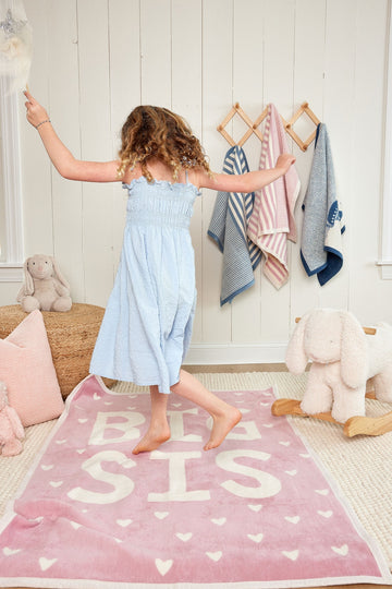 Pink midi blanket with "BIG SIS" text and white hearts, displayed on floor with child.4