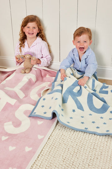 Two children holding mini blankets: pink with white text pattern and blue with white stars and text pattern.3