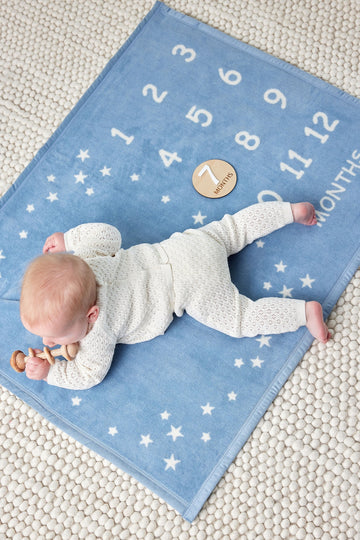 Blue milestone blanket with white stars and numbers, baby in cream sweater on blanket with coin marker.4