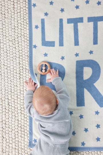 Cream and blue blanket with scattered stars and "LITTLE BRO" text, shown with infant from above.2