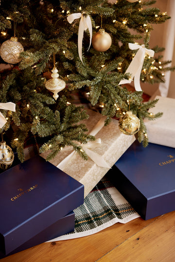 Tan and black plaid tree skirt with cream ribbon bows around decorated evergreen base.