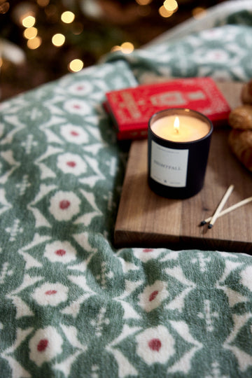 Green and white floral patterned blanket with red and pink flowers displayed with a lit candle and red book.4