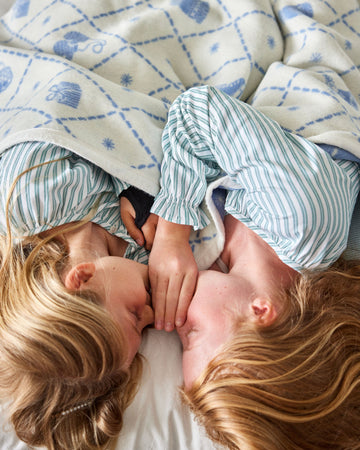 Two children in striped pajamas lying on cream blanket with blue botanical print pattern.5