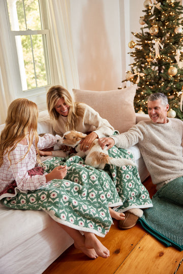Green and cream floral patterned blanket draped over a family and dog on a bed by a Christmas tree.3