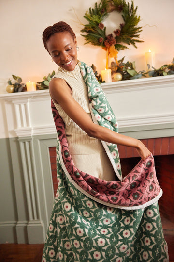 Green and burgundy floral blanket with white trim draped over woman's shoulder.5