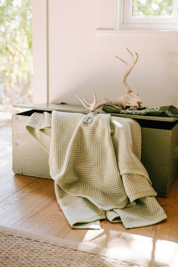 Green and cream herringbone patterned blanket draped over a wooden trunk indoors.6
