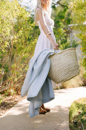 Light blue herringbone-patterned blanket draped over a woven basket, held by a person in a white dress.2