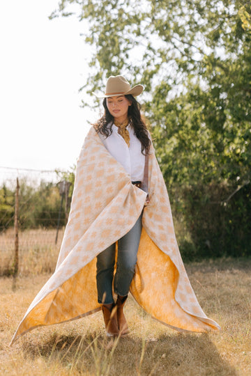 Cream and golden houndstooth patterned blanket draped around woman in outdoor field setting.5