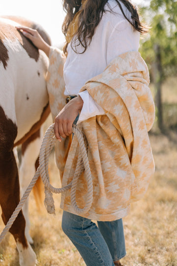 Gold and cream patterned lightweight blanket draped over person's shoulders holding a rope near a horse.6