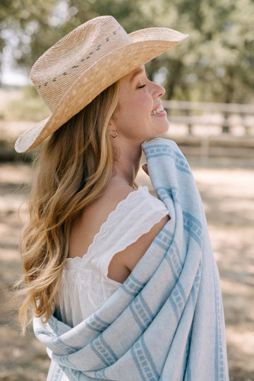 Light blue and white striped lightweight blanket draped over woman's shoulders outdoors.2