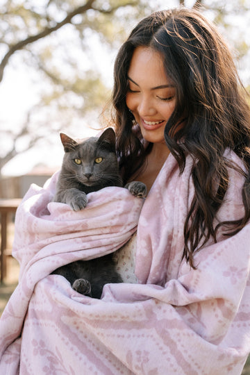 Light pink floral blanket wrapped around a woman holding a gray cat outdoors.4