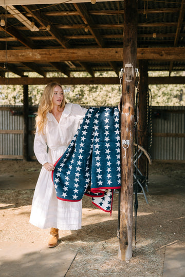 Navy blue blanket with white stars and red trim displayed on wooden post in barn setting.2