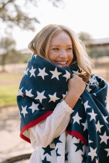 Navy blue blanket with white stars and red stripe border, draped around child's shoulders outdoors.6