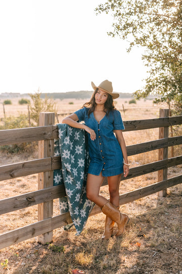 Teal and white star-patterned lightweight blanket draped over wooden ranch fence in desert landscape.6