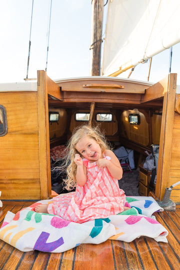Child sitting on white blanket with colorful ABC letters on wooden boat deck.4