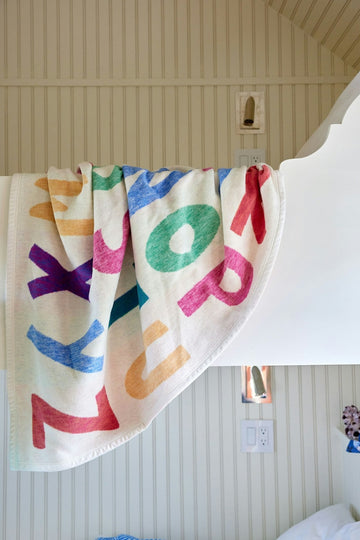 Cream blanket with multicolored alphabet letters draped over white bed frame in bedroom.2