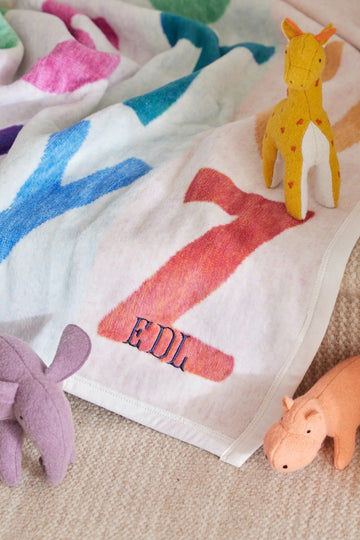 Cream blanket with colorful animal silhouettes in pink, blue, red, and purple, displayed with matching stuffed toys.3