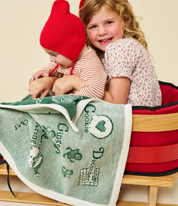 Green and white mini blanket with Christmas alphabet design and holiday graphics, held by two children.3