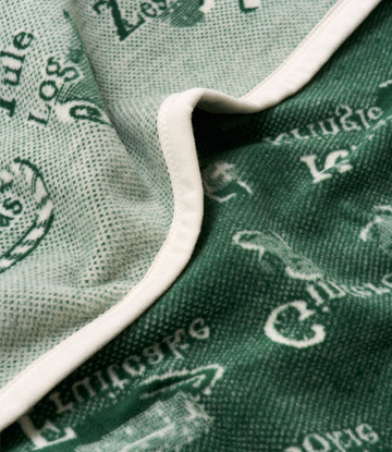 Green and cream knit blanket with white trim showing alphabet and Christmas-themed pattern details.4