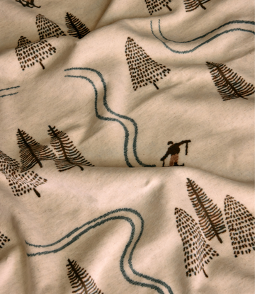 Cream blanket with embroidered forest pattern featuring trees, winding paths, and a small figure in brown and teal.3