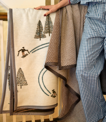 Cream blanket with skier and pine tree design in brown and teal, herringbone pattern reverse side.5