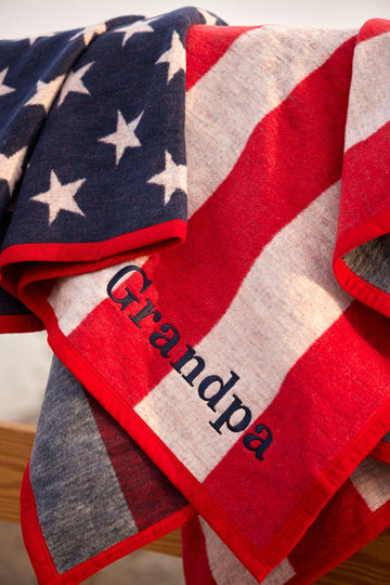 Folded blanket featuring blue field with white stars and red and white stripes in American flag design with text label on edg5