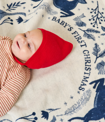 Infant wrapped in red knit hat on cream blanket with navy botanical print and "Baby's First Christmas" text.5