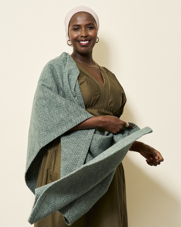 Green herringbone woven shawl draped over olive dress, shown on model against neutral background.7