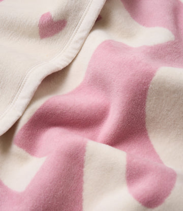 Cream and pink blanket with heart pattern and white binding along the edge.3