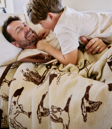 Cream blanket with brown bird dog print patterns, draped over adult and child on bed.2