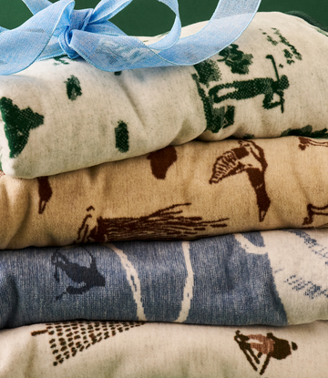 Stacked folded blankets with dog and hunting-themed patterns in cream, green, brown, and blue, tied with light blue ribbon.5