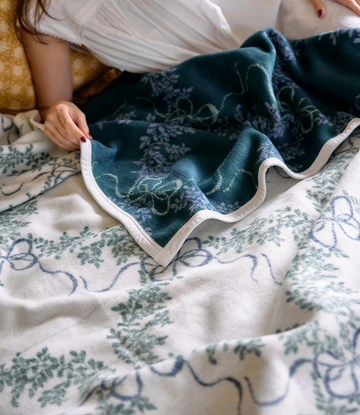 Teal and cream blanket with boxwood wreath pattern, displayed folded with cream binding along edges.4