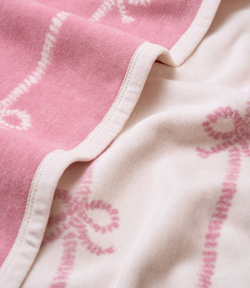 Pink and white blanket with bow pattern and white binding edge, shown folded.4