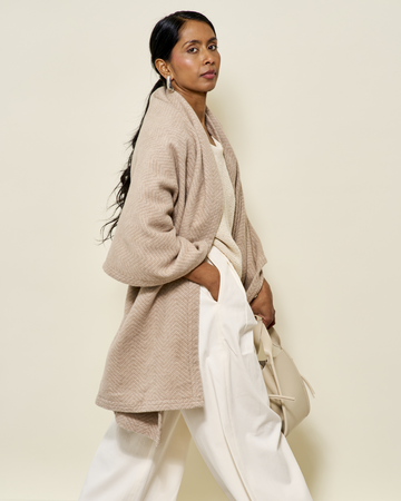 Wheat-colored herringbone shawl with textured weave draped over shoulders, worn with white pants.6