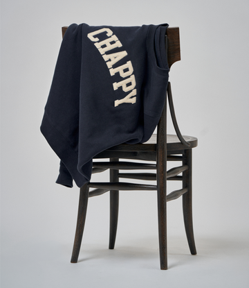 Navy crewneck sweatshirt with cream "CHAPPY" text draped over a wooden chair.4