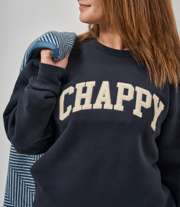 Navy crewneck sweatshirt with cream "CHAPPY" text and blue striped sleeves on model.2
