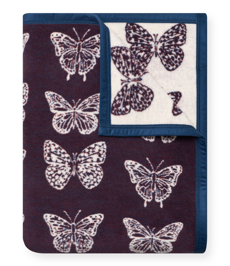 Folded blanket with burgundy side featuring white butterfly pattern and cream reverse side with navy border.