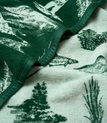 Green and cream blanket with fish and evergreen tree jacquard pattern, showing binding detail and layered fold.5