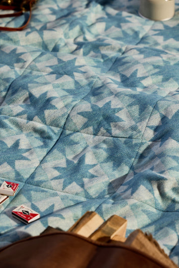 Blue and white star-patterned outdoor blanket laid flat with games and beverages on top.4