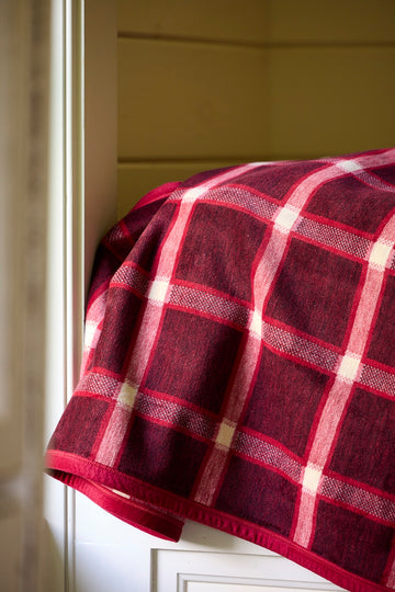 Burgundy and pink plaid blanket with cream-colored grid lines draped over a white railing.4