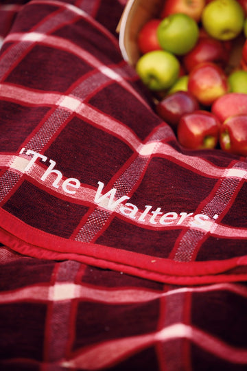 Red and white plaid blanket with woven text detail, displayed with apples in background.6