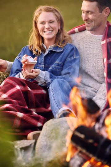 Red and black plaid blanket draped over couple sitting by campfire.2