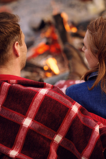 Red and white plaid blanket draped over a person's shoulders near a campfire.3
