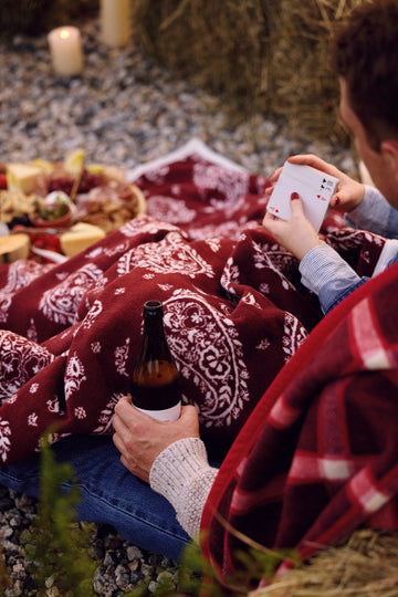 Burgundy blanket with white paisley pattern spread on ground during outdoor picnic gathering.5