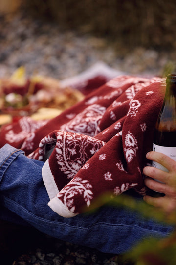 Burgundy blanket with white paisley pattern draped over person's lap outdoors.3