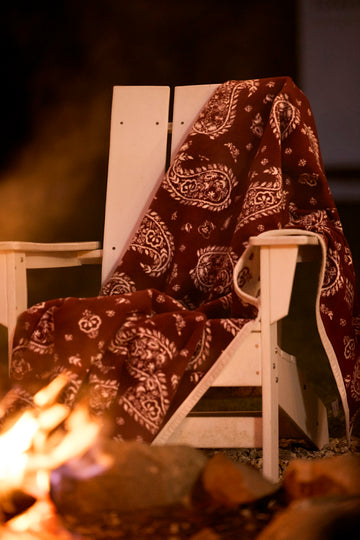 Burgundy blanket with cream paisley pattern draped over a wooden chair next to a fireplace.4