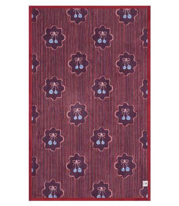 Red midi blanket with repeating pattern of dark burgundy star-shaped medallions containing blue cherry pairs and pink bows.10