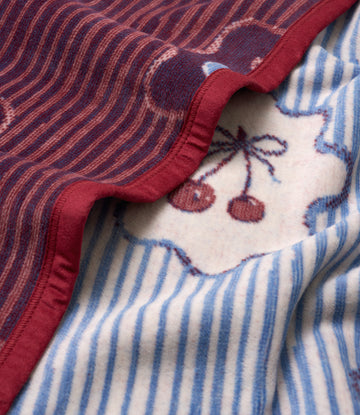 Folded blanket with burgundy wavy pattern on top, cream and blue striped section below with embroidered cherry design and red8